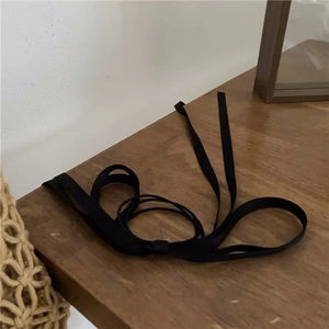 Detail of a long black satin ribbon hair tie accessory placed on a wooden tabletop