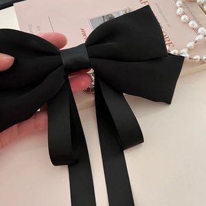 Close-up of elegant black ribbon bow hair clip held by hand with pearl necklace decor