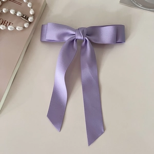 Detail view of light purple satin bow hair clip with long streamers on silk fabric