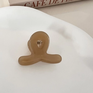Detailed view of amber acetate mini hair claw clip with golden metal spring on white tray