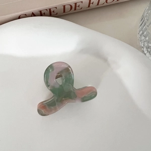 Mini acetic acid hair claw clip with colorful marble pattern on a ceramic tray