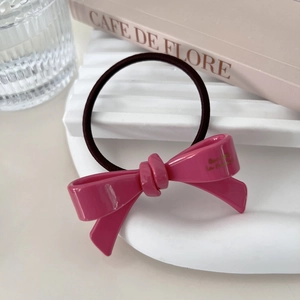 Detail of pink resin bow hair tie with gold lettering on white wavy display stand