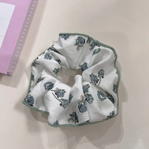 Detail of floral scrunchie featuring blue roses and green stitched edges on white fabric