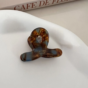 Detail view of mini acetate hair claw with amber marble texture on white wavy tray