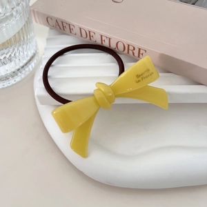 Close-up of yellow acetate bow hair tie with French Barrette engraving on white display