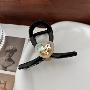 Elegant black heart-shaped hair claw clip with colorful rhinestones on a ceramic dish