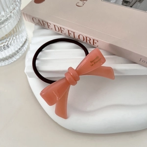 Detail of coral acetate bow hair tie with golden script on a French aesthetic background