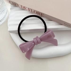 Detail of purple acetate bow hair tie with golden logo on a white aesthetic tray