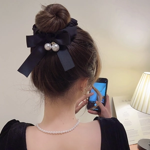 Close-up of black satin bow hair tie with pearl accents on a bun hairstyle
