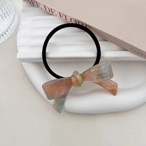Detail of pink and blue gradient bow hair tie with gold lettering on a white tray