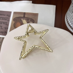 Detail of gold star-shaped hair claw with textured surface on a white ceramic stand
