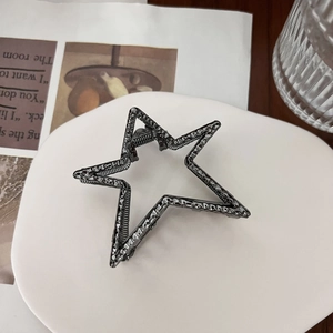 Macro detail of star-shaped hair claw with hammered metallic texture and dark gunmetal finish