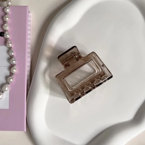 Translucent brown rectangular hair claw clip on a white ceramic tray with pearls