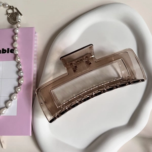 Close-up of a translucent coffee-colored rectangular claw clip on a white ceramic plate