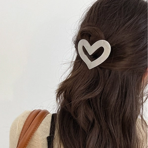 Detailed view of a silver heart-shaped metal hair clip on wavy brown hair for women