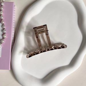 Detail of amber translucent claw clip with metal spring on a white ceramic tray