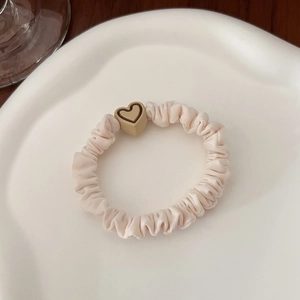 Close-up of beige ruffled scrunchie with heart-shaped resin bead on ceramic tray