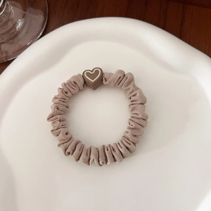 Detail of cream pleated hair scrunchie with brown heart bead on a white ceramic plate