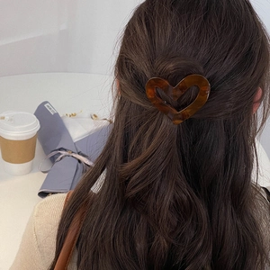 Detail of a brown tortoiseshell heart hair clip worn on long wavy hair in a cozy setting