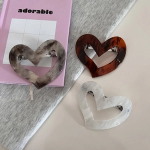 Detail of three acetate hollow heart hair clips with marble texture on pink books