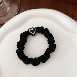 Detail of black elastic hair scrunchie with heart charm on a white ceramic tray
