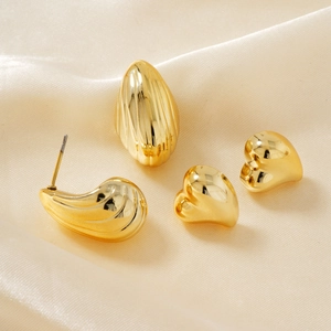 Macro detail of gold geometric teardrop and heart earrings on beige satin fabric