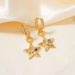 Detalle de pendientes de estrella dorados con micro-pavé de circonitas sobre seda champán
