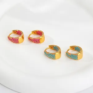 Dettaglio di orecchini huggie dorati con micro-set di cristalli rosa e blu su vassoio bianco