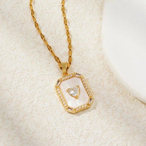 Goldene Halskette mit Herz-Zirkonia-Anhänger auf weißem Muschelboden im minimalistischen Stil