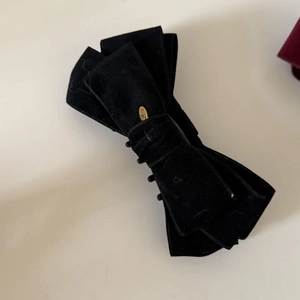 Detail of elegant black velvet bow hair clip with engraved gold oval metal tag