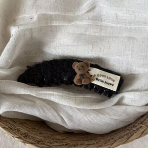 Detail of black plush claw clip with a brown bear plush and a Good Luck woven label