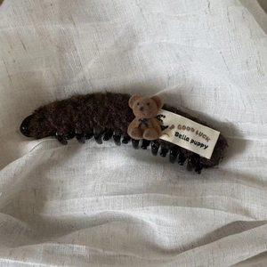 Detailed close-up of brown plush banana hair clip with cute flocking bear and Good Luck tag