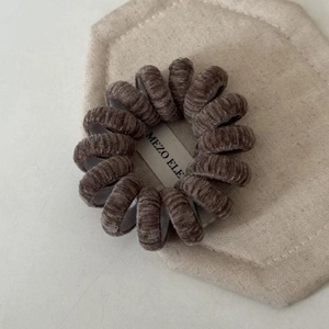 Détail d'un élastique spirale en velours taupe avec une étiquette en tissu de marque