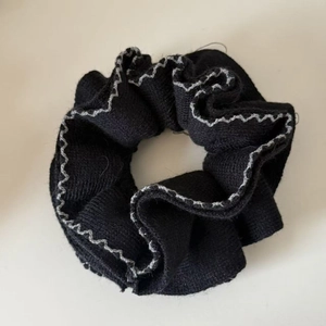 Détail du chouchou en maille noire avec des bords ondulés à surpiqûres grises