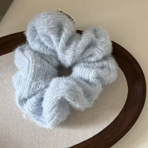 Detailed close-up of a soft light blue plush knit scrunchie on a wooden tray