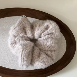 Close-up of fuzzy knit hair scrunchie in pale purple with soft plush texture on wood tray