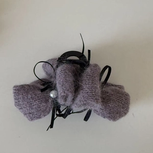 Dettaglio della molletta per capelli in peluche viola con fiocchi neri e perla bianca