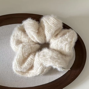 Macro shot of cream white plush knitted scrunchie texture in a dark wooden tray