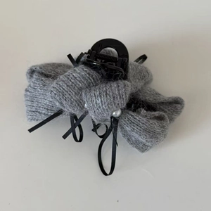 Dettaglio della pinza per capelli in maglia grigia con nastri neri e perle bianche eleganti