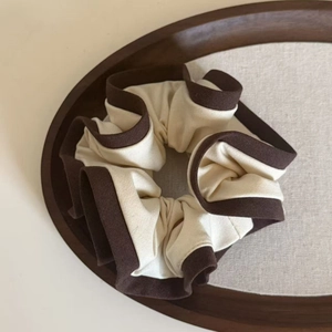 Brown bordered cream scrunchie with floral petal ruffles on a wooden tray