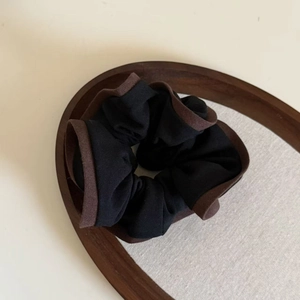 Close-up of black and brown vintage scrunchie on a wooden tray with linen background
