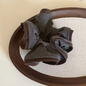 Detail of grey and brown cotton scrunchie on a wooden tray with soft natural lighting