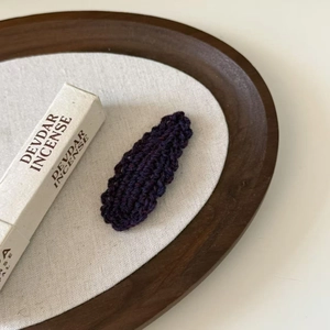 Macro detail of hand-knitted wavy wool hair clip in deep purple on a rustic tray