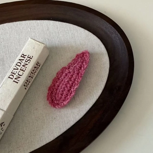 Close-up of a handmade magenta crochet water-drop hair clip on a rustic linen background