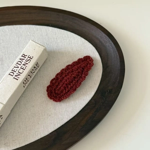 Close-up of a handmade dark red wave knit wool teardrop hair clip with soft texture