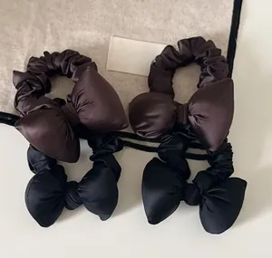 Flat lay of satin bow scrunchies in dark brown and black silk-like fabric texture