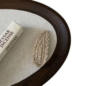 Handmade wavy knit wool waterdrop hair clip in beige, placed on a rustic wooden tray