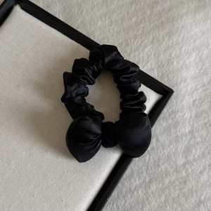 Detail of a black satin scrunchie with a ribbon bow on a white textured board