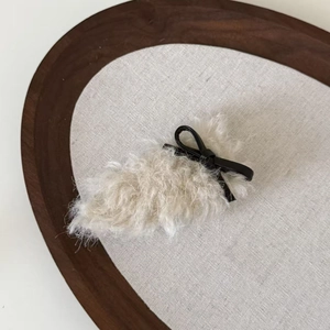 Plush faux shearling bow hair clip in cream and black on a minimalist wooden tray
