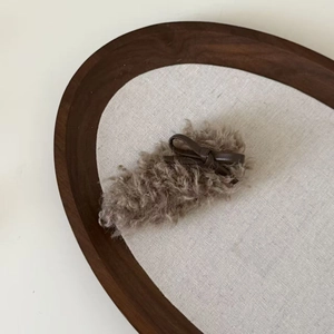 Detail of plush lamb wool hair clip with a dark brown faux leather bow on a tray